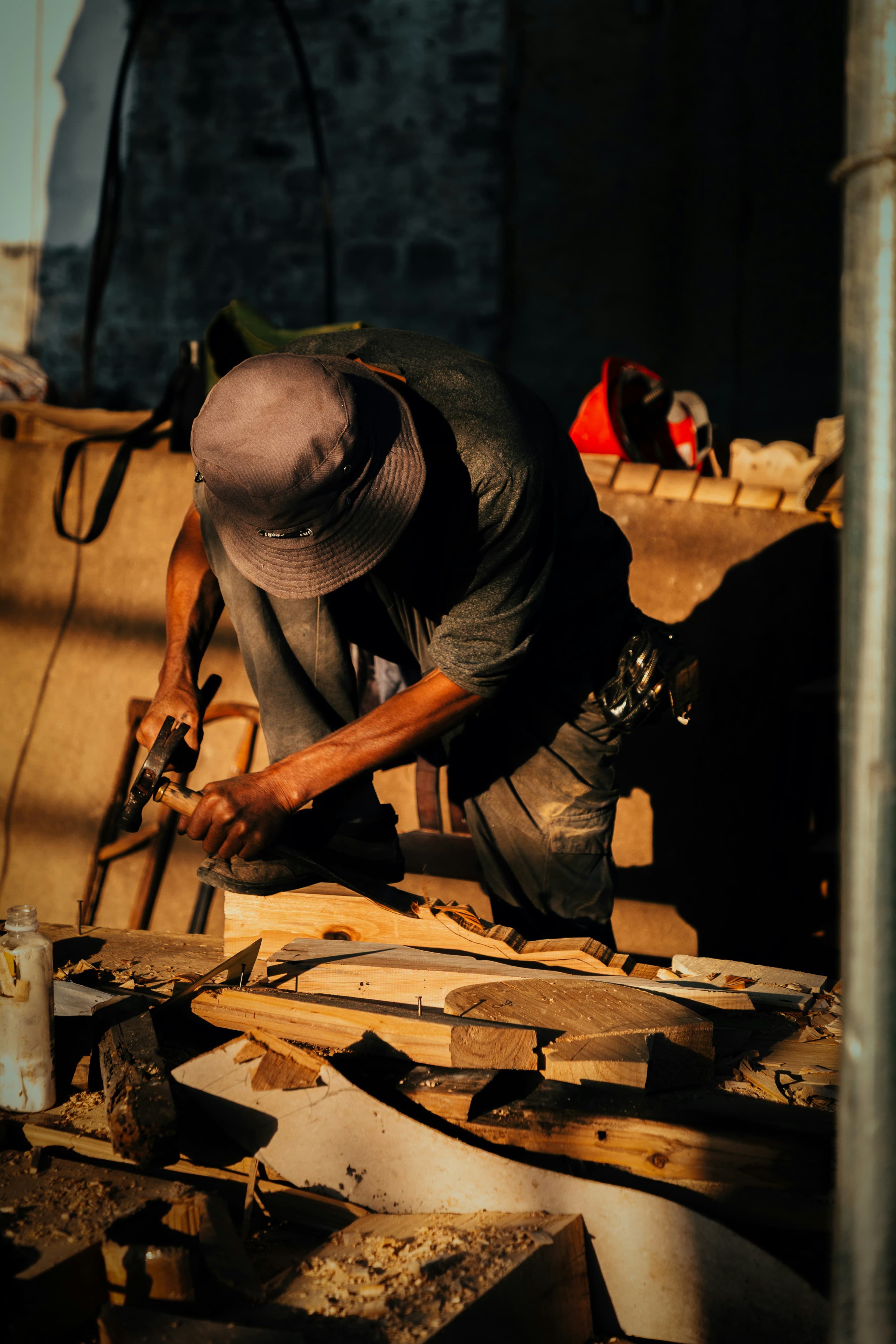 A carpenter shaping timber with a hammer and chisel in warm workshop light